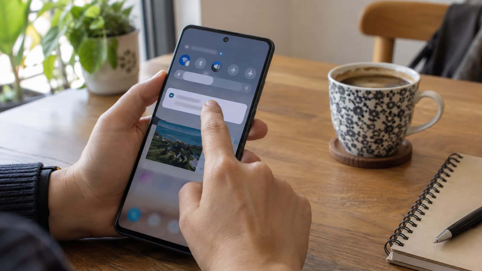Bir el, Samsung telefon ekranındaki bildirimi ekranın ortasına doğru sürüklüyor; arka planda ahşap masa ve kahve fincanı var.