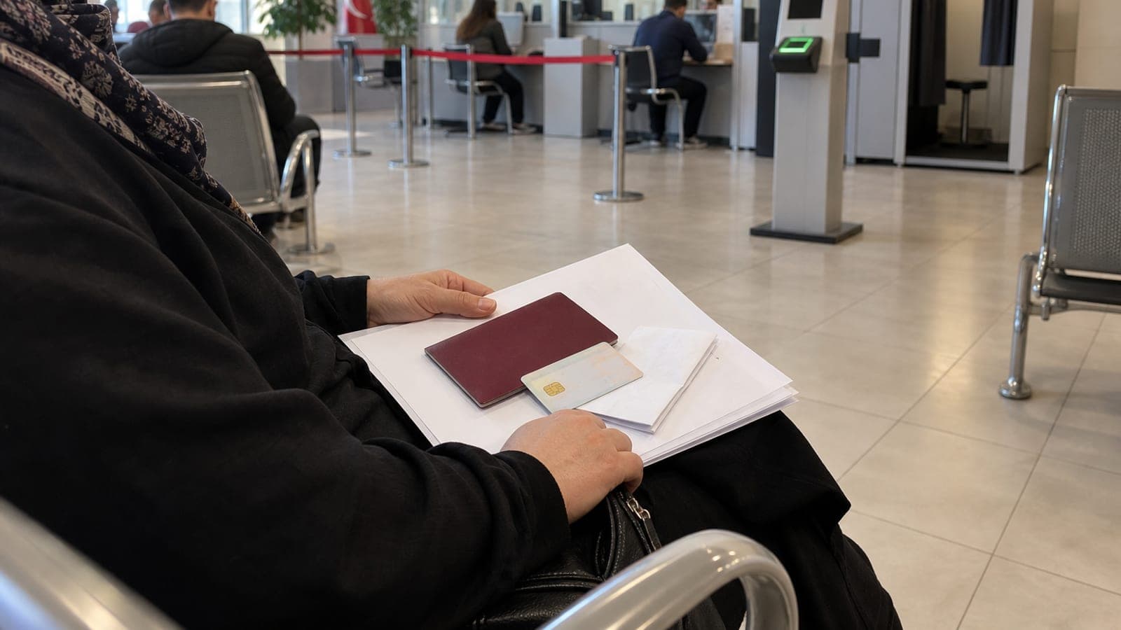 Nüfus müdürlüğü bekleme salonunda dosyası, pasaportu, kimliği ve ödeme dekontuyla sırasını bekleyen bir kadın