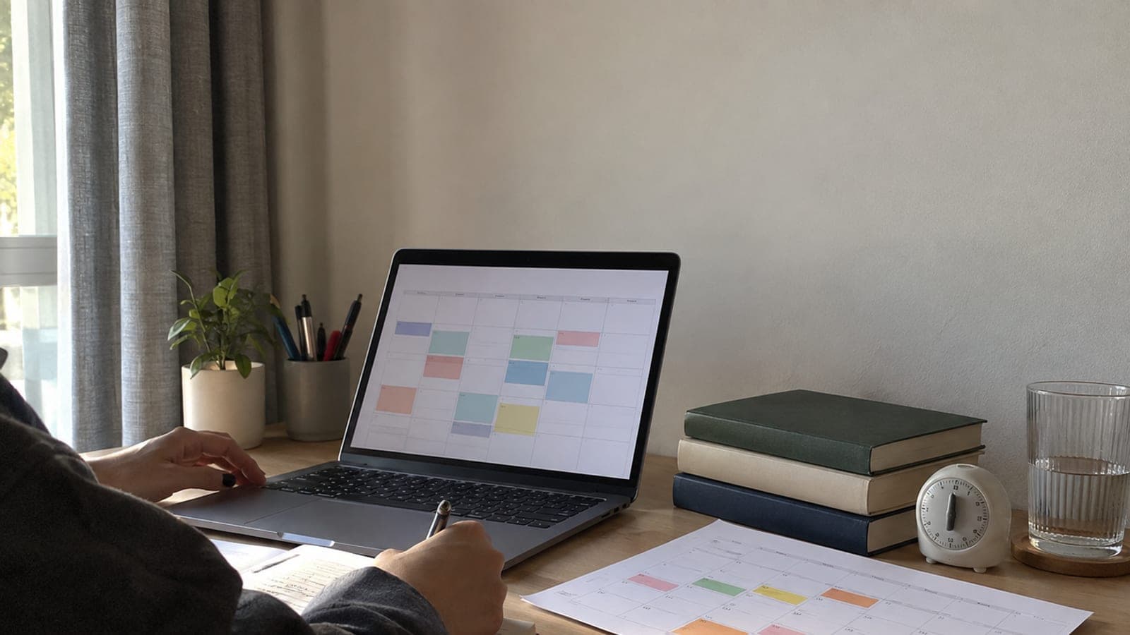 Dizüstü bilgisayarda haftalık takvim, renkli işaretlenmiş basılı takvim, zamanlayıcı ve ders kitaplarının bulunduğu düzenli çalışma masası